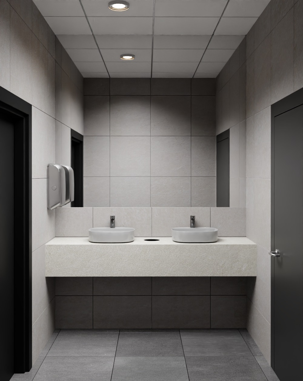 Nowoczesna łazienka publiczna z dwoma okrągłymi umywalkami na blacie z jasnego kamienia. Szare płytki na ścianach i podłodze, duże lustro, czarne drzwi i dyspenser do ręczników.