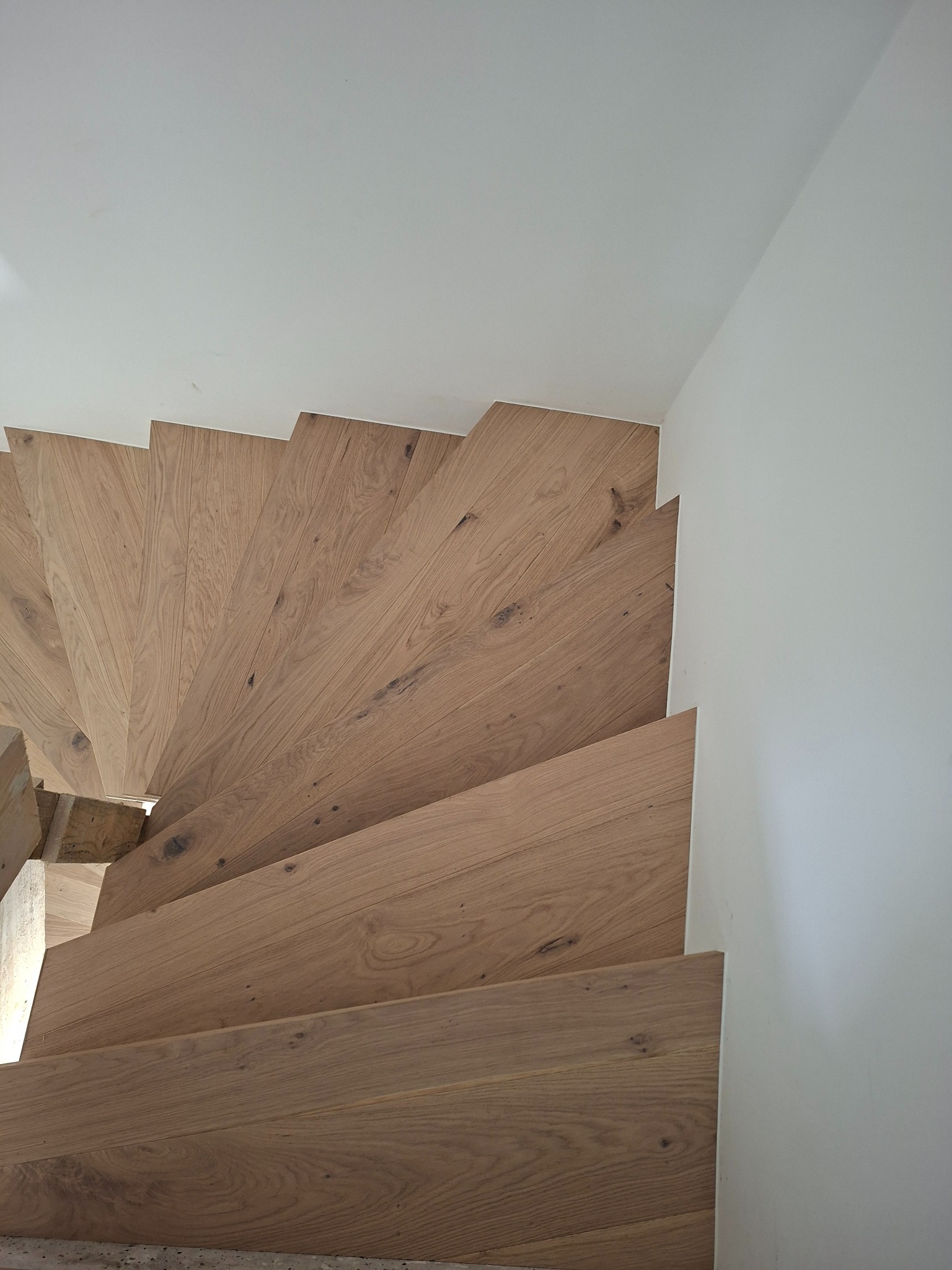 Drewniane schody spiralne z jasnego drewna dębowego, widok z góry, białe ściany, nowoczesny design, detale wykończenia, naturalne oświetlenie.