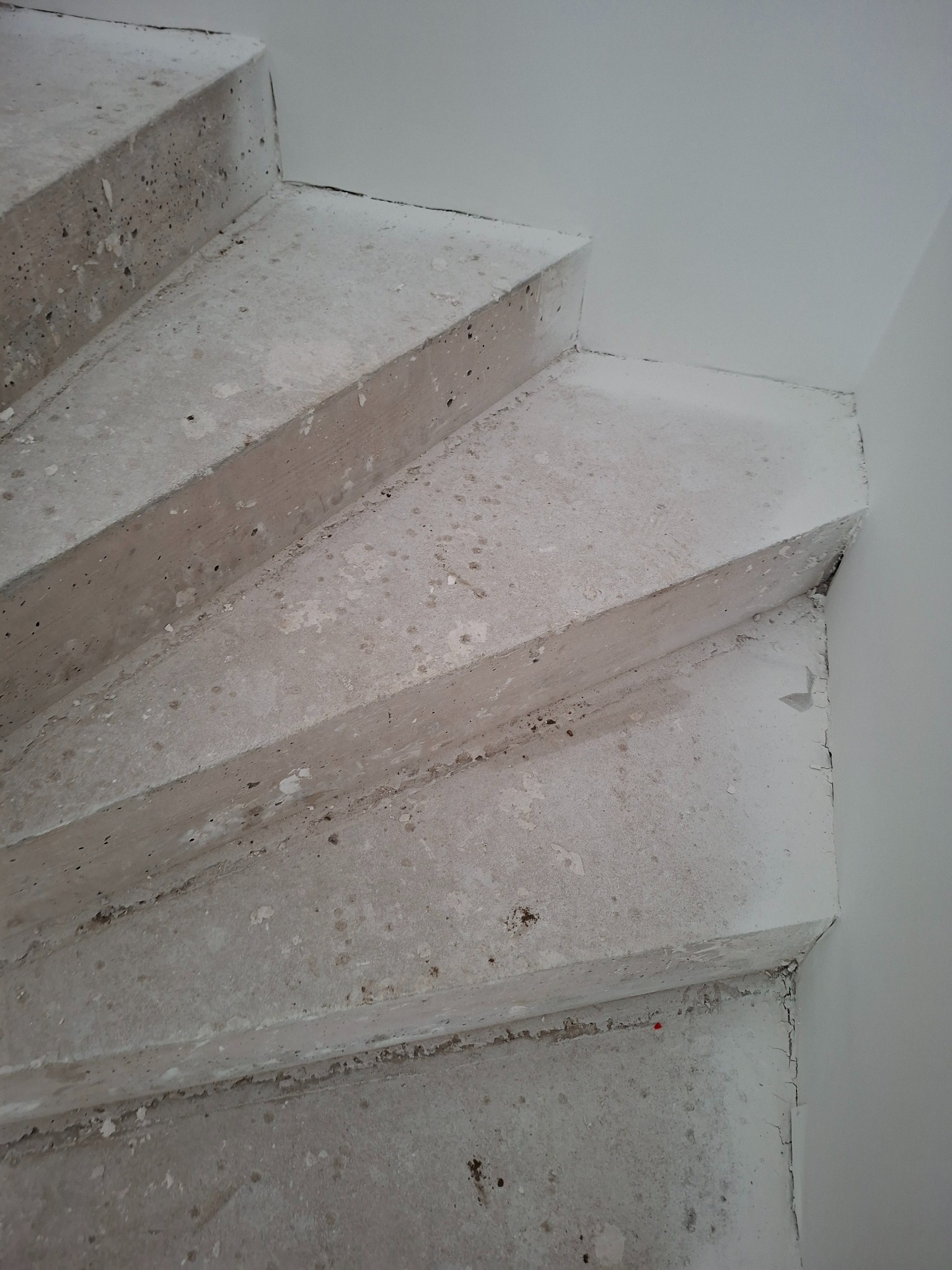 Surowe, betonowe schody w trakcie wykończenia, widoczne niedoskonałości i przygotowanie do dalszych prac. Minimalistyczne ujęcie z bliska, ukazujące fakturę betonu.