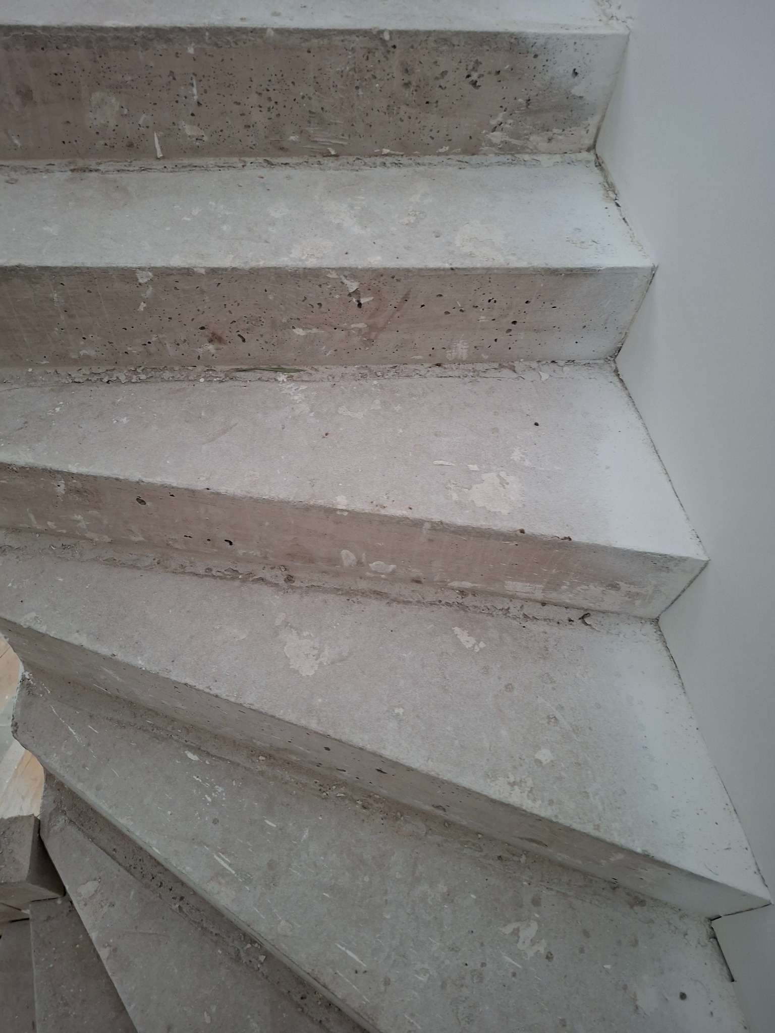 Surowe, betonowe schody spiralne w Brzyskiej, z widoczną fakturą betonu i fragmentem białej ściany. Ujęcie z dołu, podkreślające geometrię stopni.