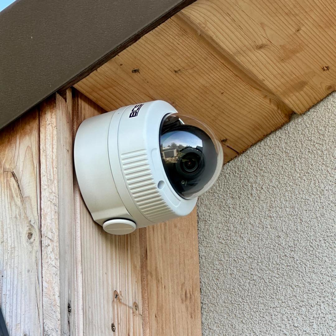 Kopułkowa kamera monitoringu BCS zamontowana na drewnianej elewacji pod okapem. Widoczny obiektyw i fragment otoczenia odbity w kopule.