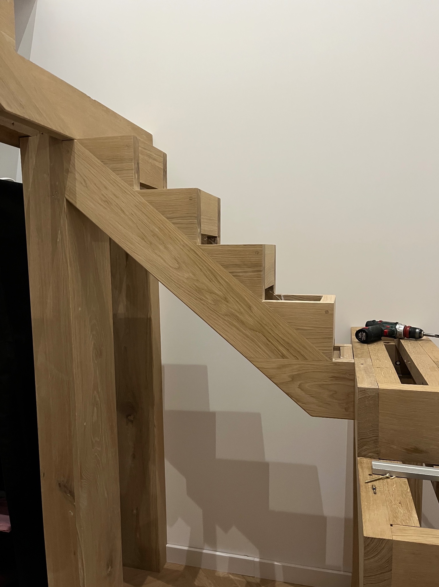 Surowe, dębowe schody w trakcie montażu, widoczne narzędzia i elementy konstrukcyjne. Jasne drewno, minimalistyczne tło.