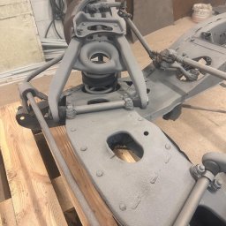 Magnaris - Szare podwozie samochodu po piaskowaniu, umieszczone na drewnianej palecie. Widoczne elementy zawieszenia i układu kierowniczego. Detaliczny widok na odnowioną konstrukcję.