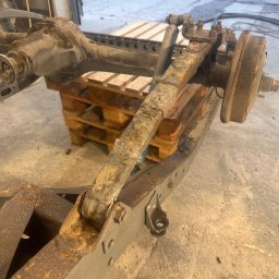 Magnaris - Zardzewiałe podwozie samochodu na palecie w warsztacie, widoczne elementy zawieszenia i mocowania. Detaliczny widok na korozję i zużycie.