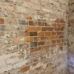 Magnaris - Ceglana ściana z widocznymi śladami starej farby i zaprawy, ukazująca surowy, industrialny charakter wnętrza. Fragment narożnika podkreśla trójwymiarowość tekstury.