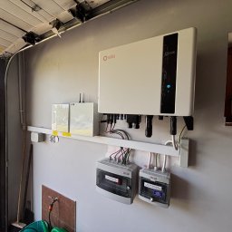 Magnaris - Biały inwerter Solis zamontowany na ścianie garażu, z widocznymi rozdzielnicami PV AC i okablowaniem. Elementy instalacji fotowoltaicznej wewnątrz budynku.