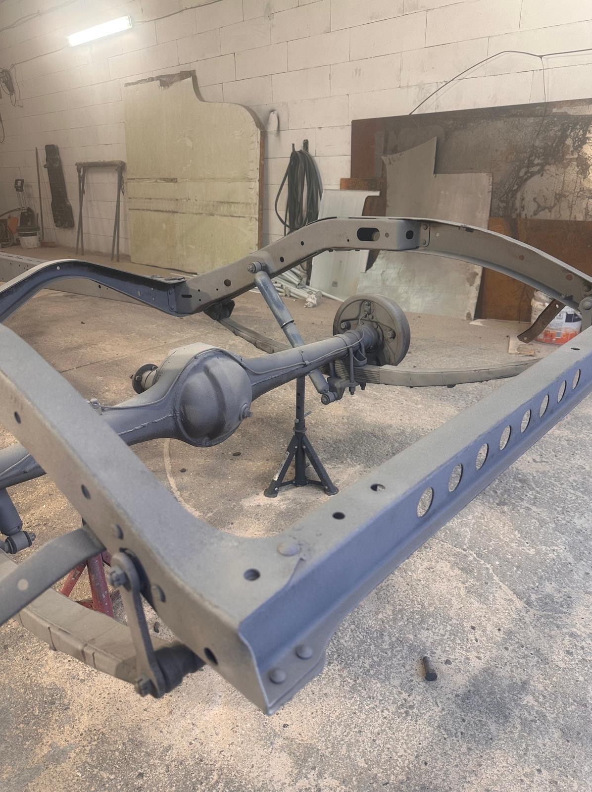 Podwozie samochodu po piaskowaniu i malowaniu proszkowym, widoczne otwory w ramie, tylny most na stojaku. Szary, matowy kolor. Warsztat.