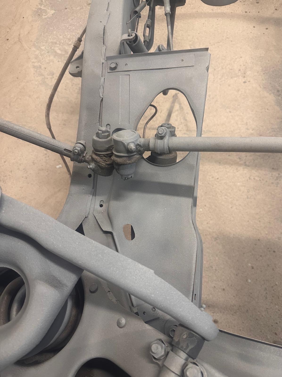 Szare, pomalowane podwozie samochodu z widocznymi elementami zawieszenia i układu kierowniczego. Detal po konserwacji antykorozyjnej, z bliska, w warsztacie.