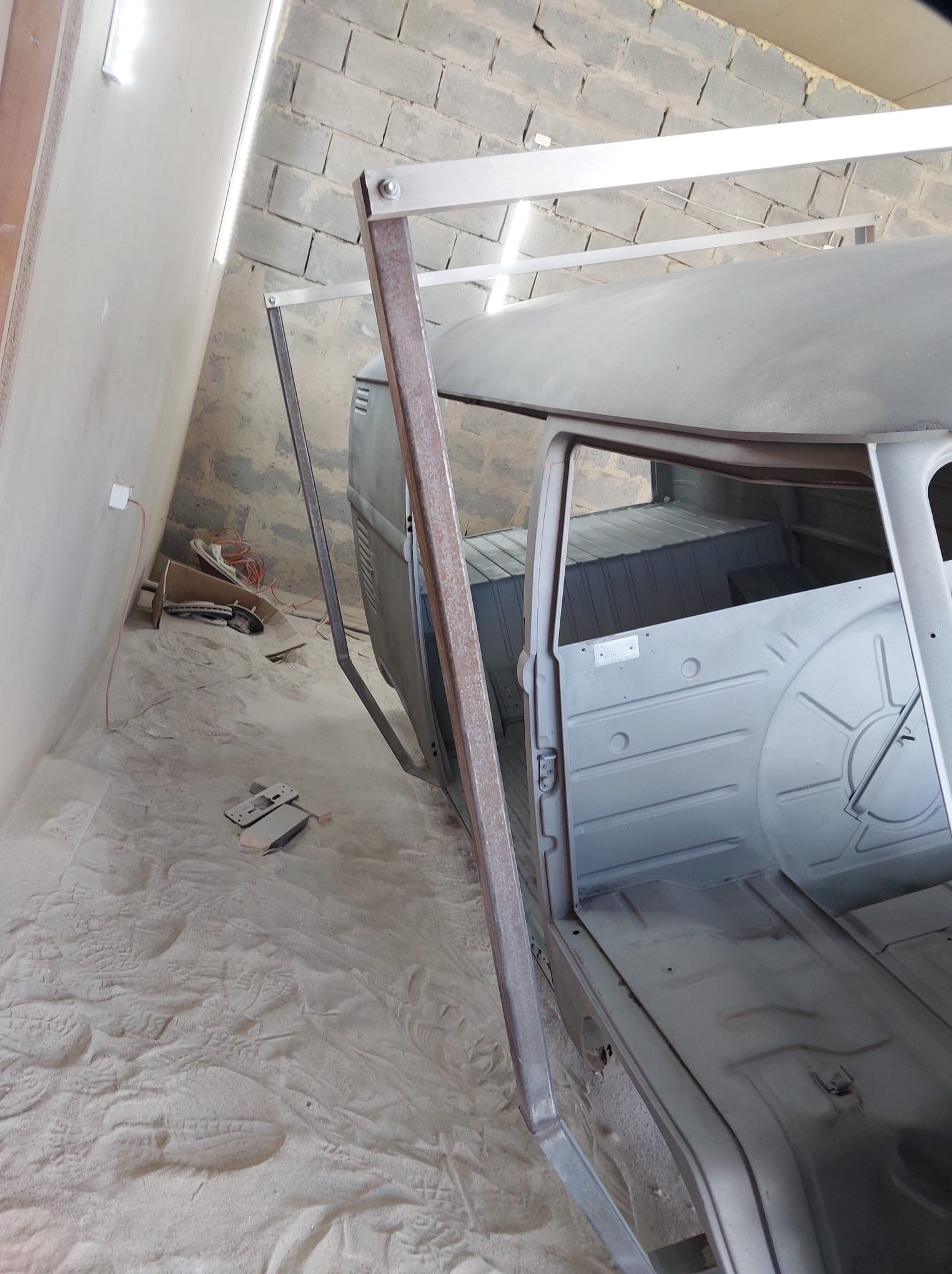 Wnętrze busa w trakcie renowacji, pokryte szarym podkładem antykorozyjnym. Widoczne elementy konstrukcyjne i podłoga. Ślady piasku na podłodze i ścianach.