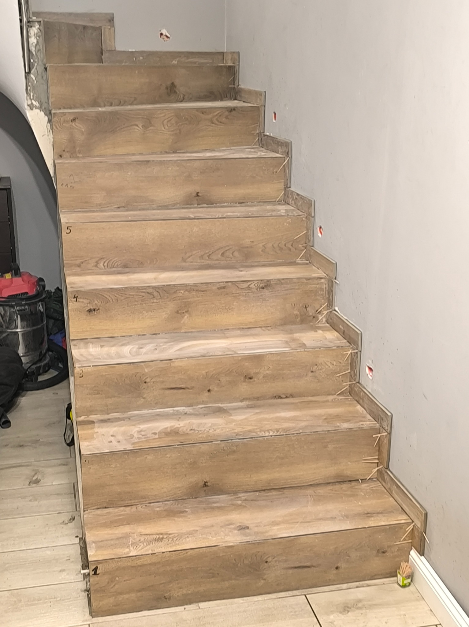 Montaż drewnopodobnych płytek na schodach w Osówcu. Widoczne numerowane stopnie i szpary wypełnione patyczkami. Prace wykończeniowe w trakcie realizacji.