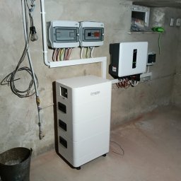 TECHMAR - Zestaw fotowoltaiczny w piwnicy: biały akumulator Dyness, inwerter, rozdzielnice elektryczne z okablowaniem. Instalacja w surowym pomieszczeniu.