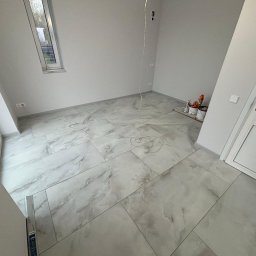 Adaro - Jasne, marmurowe płytki podłogowe w nowym pokoju z oknem i białymi ścianami. Widoczne wiaderka z farbą i kabel zwisający z sufitu. Minimalistyczny design.