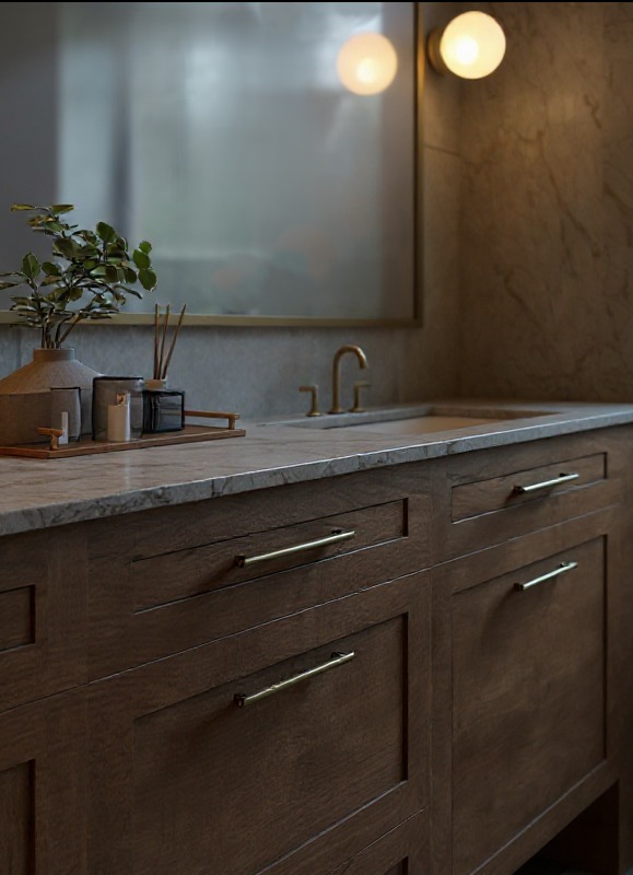 Elegancka łazienka: drewniana szafka z marmurowym blatem, złota armatura i okrągłe lampy. Minimalistyczny design z rośliną i dyfuzorem zapachowym.