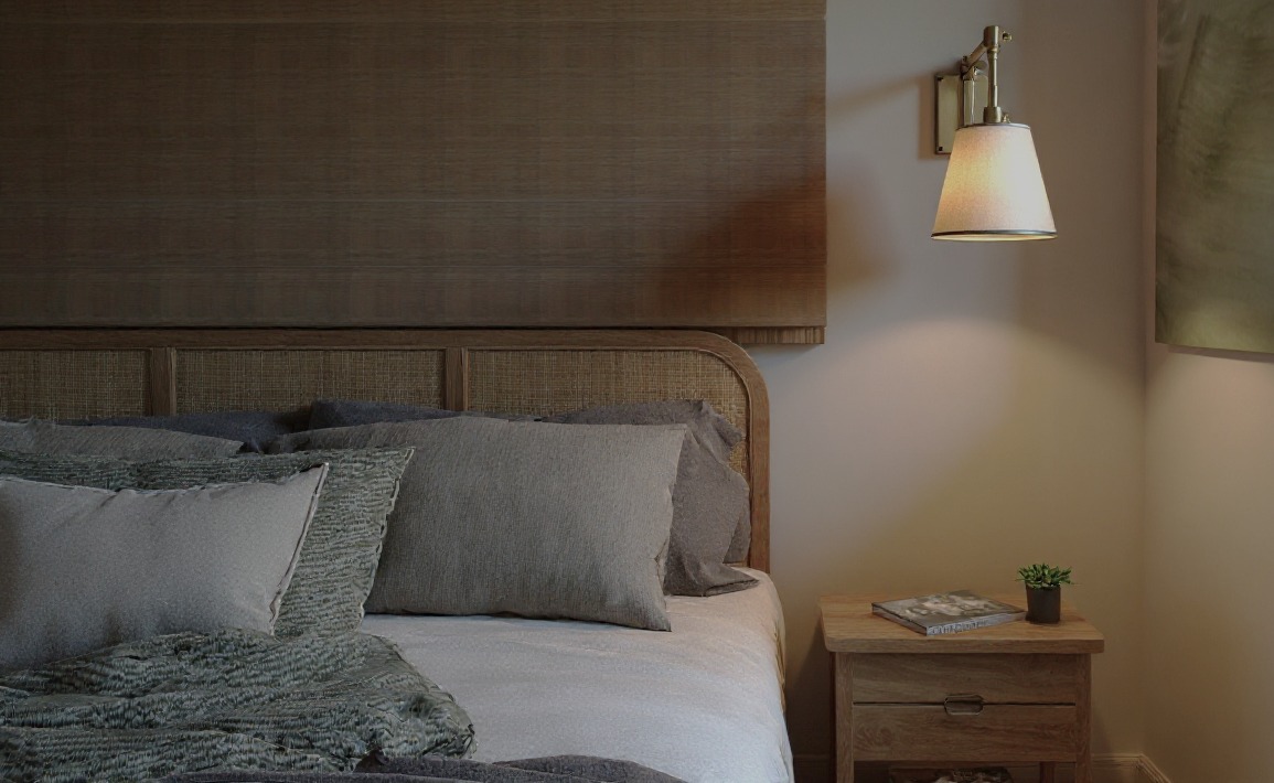 Sypialnia w neutralnych barwach: rattanowe wezgłowie łóżka, drewniana szafka nocna z lampką i książką, tekstylia w odcieniach szarości. Przytulne wnętrze.