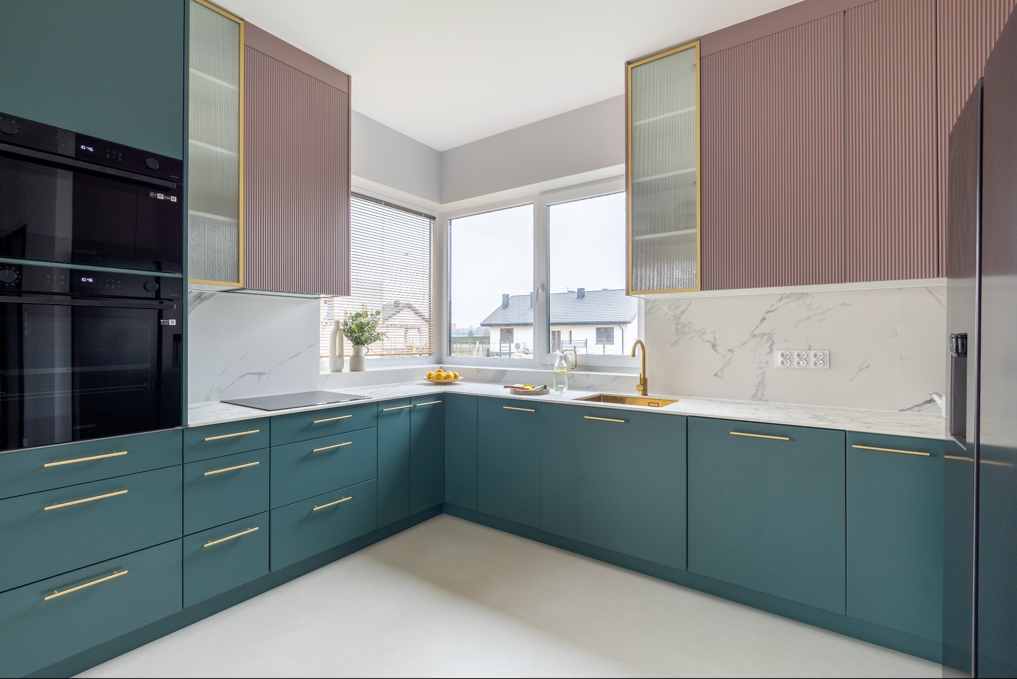 Nowoczesna kuchnia w odcieniach zieleni i różu z marmurowym blatem, złotymi akcentami i dużym oknem z widokiem na dom. Minimalistyczny design, eleganckie wykończenie.