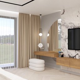 HulseyArt Projektowanie Wnętrz Katarzyna Mularska-Hulsey - Nowoczesna sypialnia z toaletką z owalnym lustrem, telewizorem na marmurowej ścianie i dużym oknem z widokiem na zieleń. Beżowe zasłony i drewniane meble dodają ciepła.