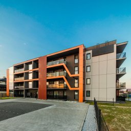 HulseyArt Projektowanie Wnętrz Katarzyna Mularska-Hulsey - Nowoczesny budynek wielorodzinny z balkonami i pomarańczowymi akcentami architektonicznymi w Rzeszowie, widziany z poziomu chodnika.