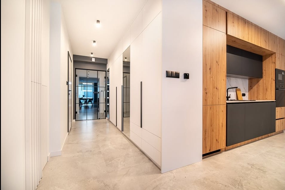 Nowoczesny korytarz z szafą wnękową z lustrami i drewnianą zabudową kuchenną z czarnymi frontami, widok na przeszklone drzwi do biura.