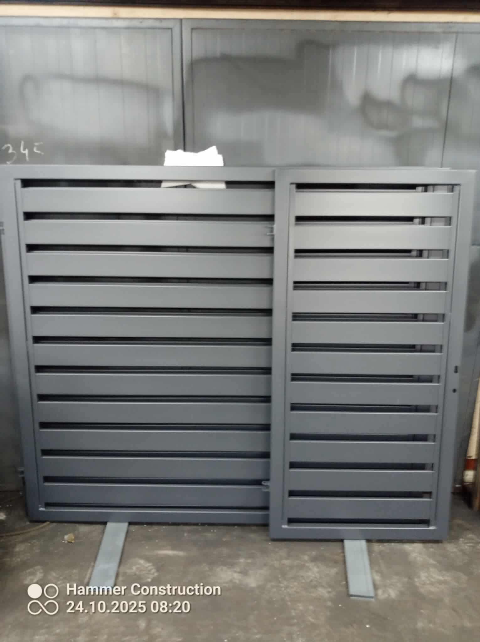 Nowoczesna, szara brama wjazdowa z poziomymi lamelami, widoczna w warsztacie przed montażem. Minimalistyczny design, surowe wykończenie, detale spawów.