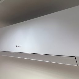 DINO TS Paweł Kwiatkowski - Biały klimatyzator Gree zamontowany na ścianie, widok z dołu, oświetlenie dzienne, minimalistyczny design.