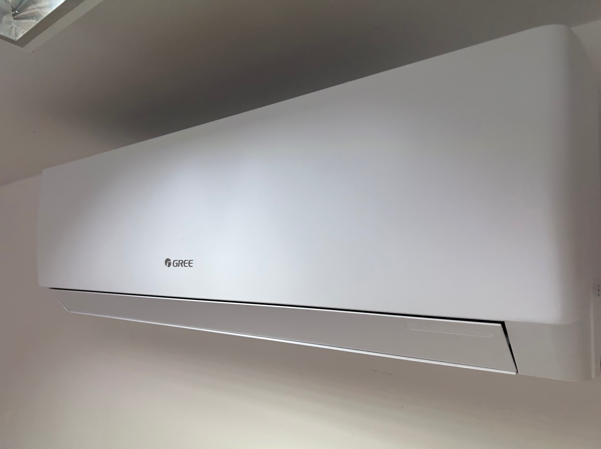 Biały klimatyzator Gree zamontowany na ścianie, widok z dołu, oświetlenie dzienne, minimalistyczny design.
