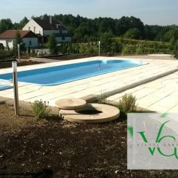 Visual Garden 5.3.0.9.0.8.7.2.8 - Kąpielowy basen z jasną kostką brukową na tarasie, otoczony zielenią i domem w tle. Widoczne studzienki kanalizacyjne i oświetlenie.