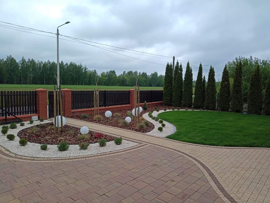 Zadbany ogród w Lubinie z trawnikiem, ścieżką z kostki, ozdobnymi kamieniami i tujami. Oświetlenie ogrodowe w postaci kul. Estetyczne wykończenie.