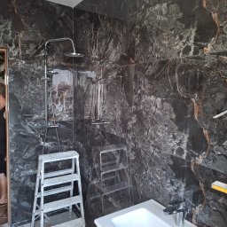 Andrzej Werner uslugi remontowo budowlane - Wykończona łazienka z czarnymi płytkami imitującymi marmur, chromowaną armaturą i drabinką. Widoczny fragment umywalki i drabina glazurnicza.