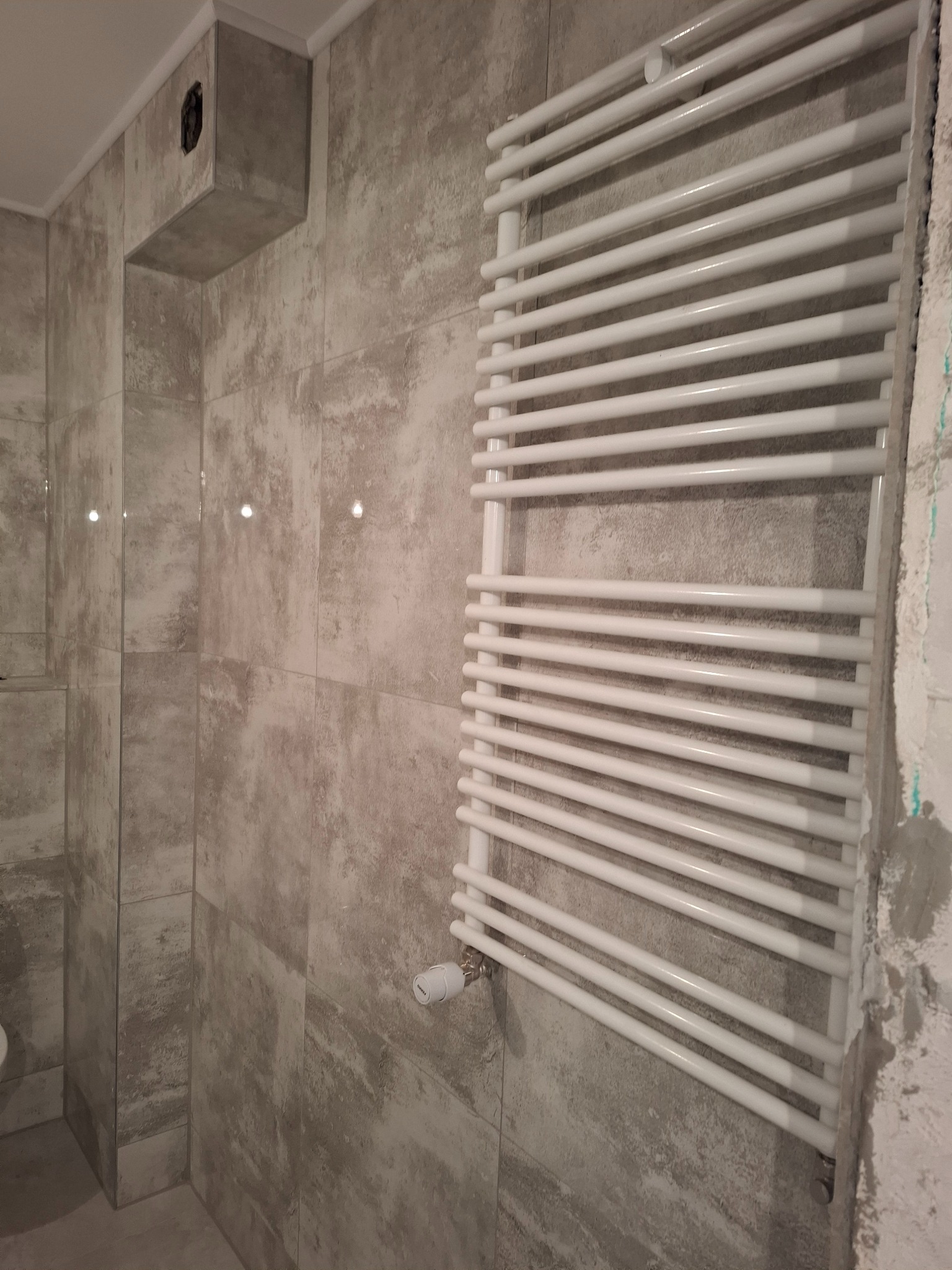 Wykończona łazienka w Dubecznie z grzejnikiem drabinkowym na ścianie z szarych płytek imitujących kamień. Widoczny fragment toalety.