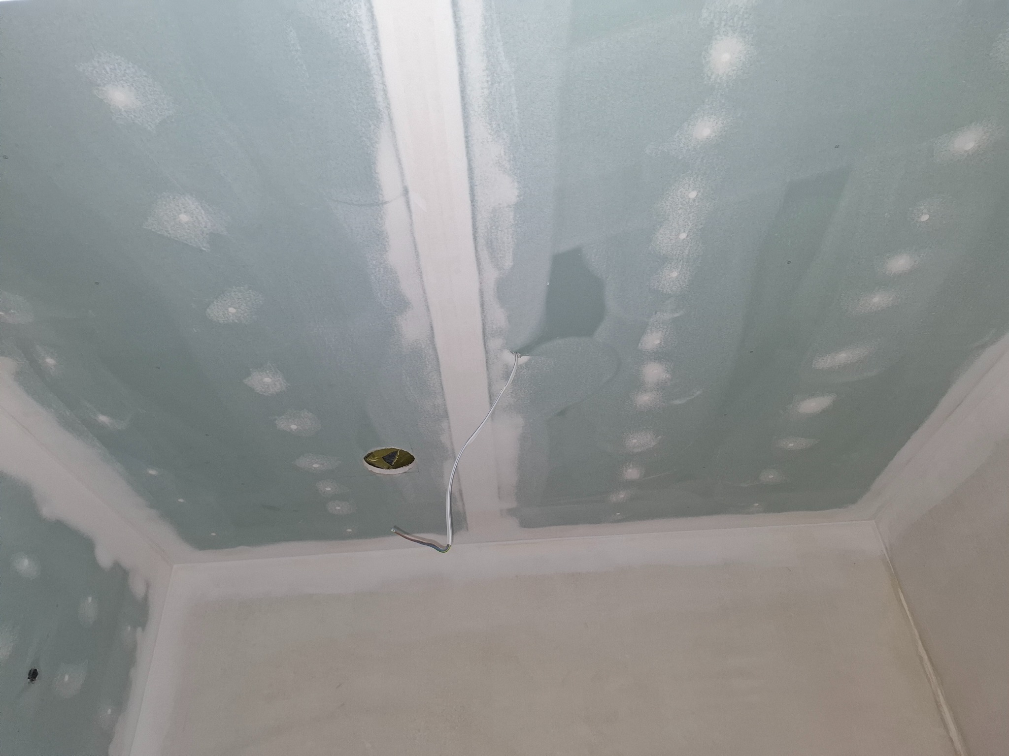 Wnętrze w trakcie szpachlowania: sufit z płyt gipsowo-kartonowych z widocznymi łączeniami i punktami szpachlowania, otwór na oświetlenie z wystającymi przewodami.