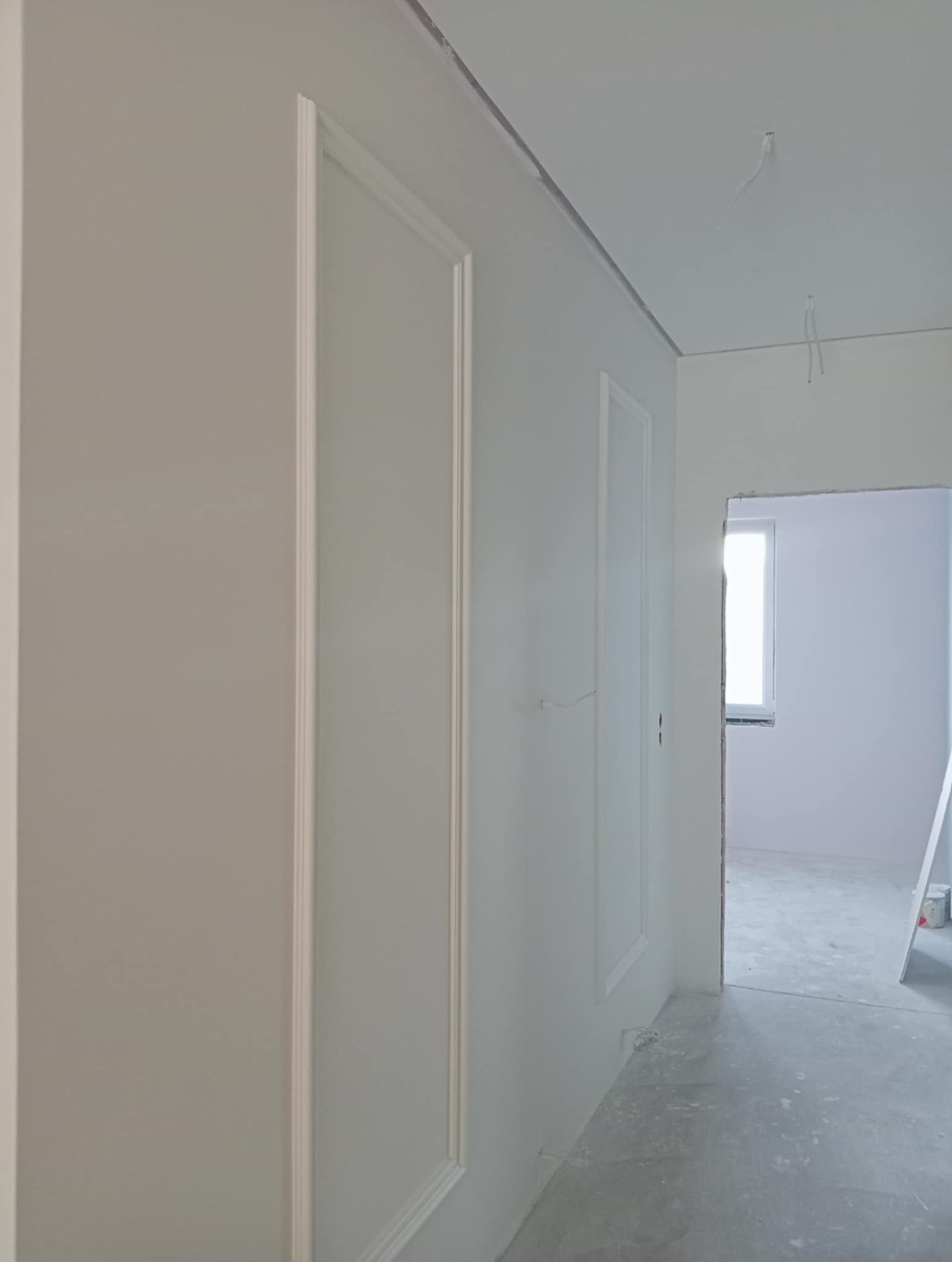 Białe ściany z dekoracyjnymi panelami w trakcie wykańczania wnętrza. Widoczne przewody elektryczne i surowa podłoga.