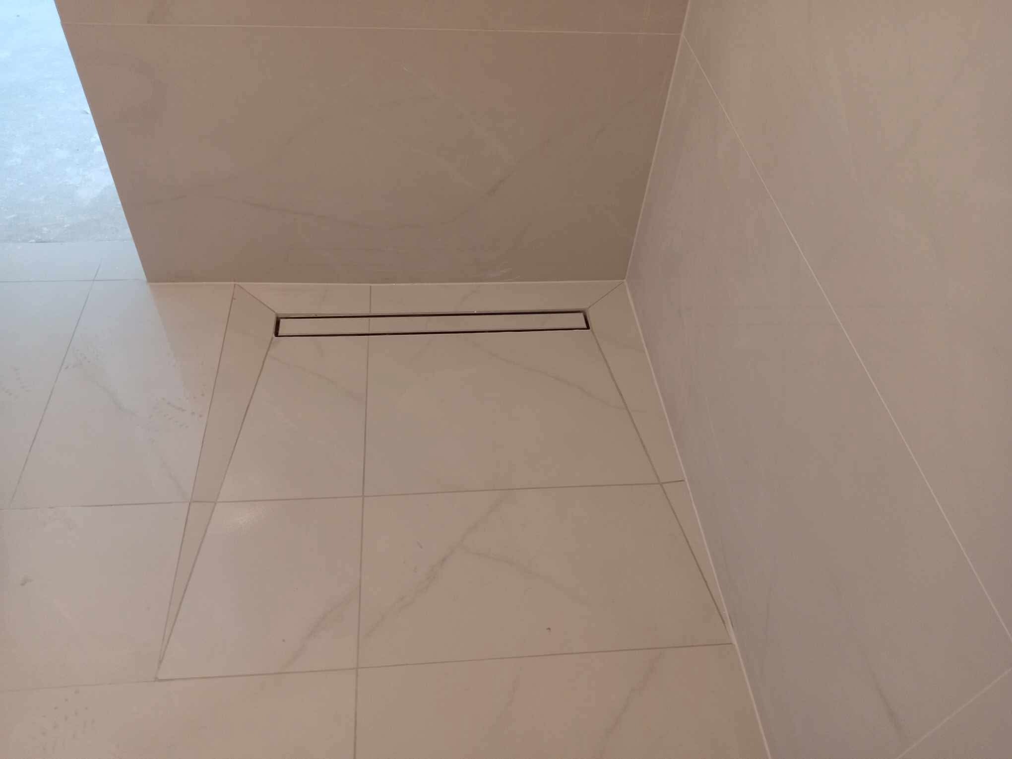 Beżowa łazienka z odpływem liniowym w kabinie prysznicowej. Płytki podłogowe i ścienne imitujące marmur. Minimalistyczny design.