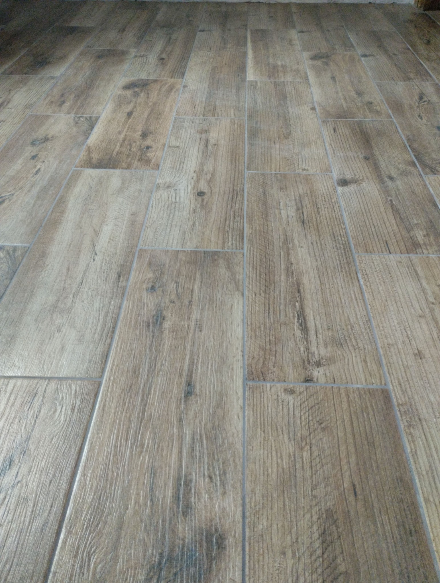 Ułożona podłoga z płytek imitujących drewno, z widocznymi fugami. Płytki ułożone w prostokątnym wzorze, z delikatnym efektem postarzenia i naturalną kolorystyką.