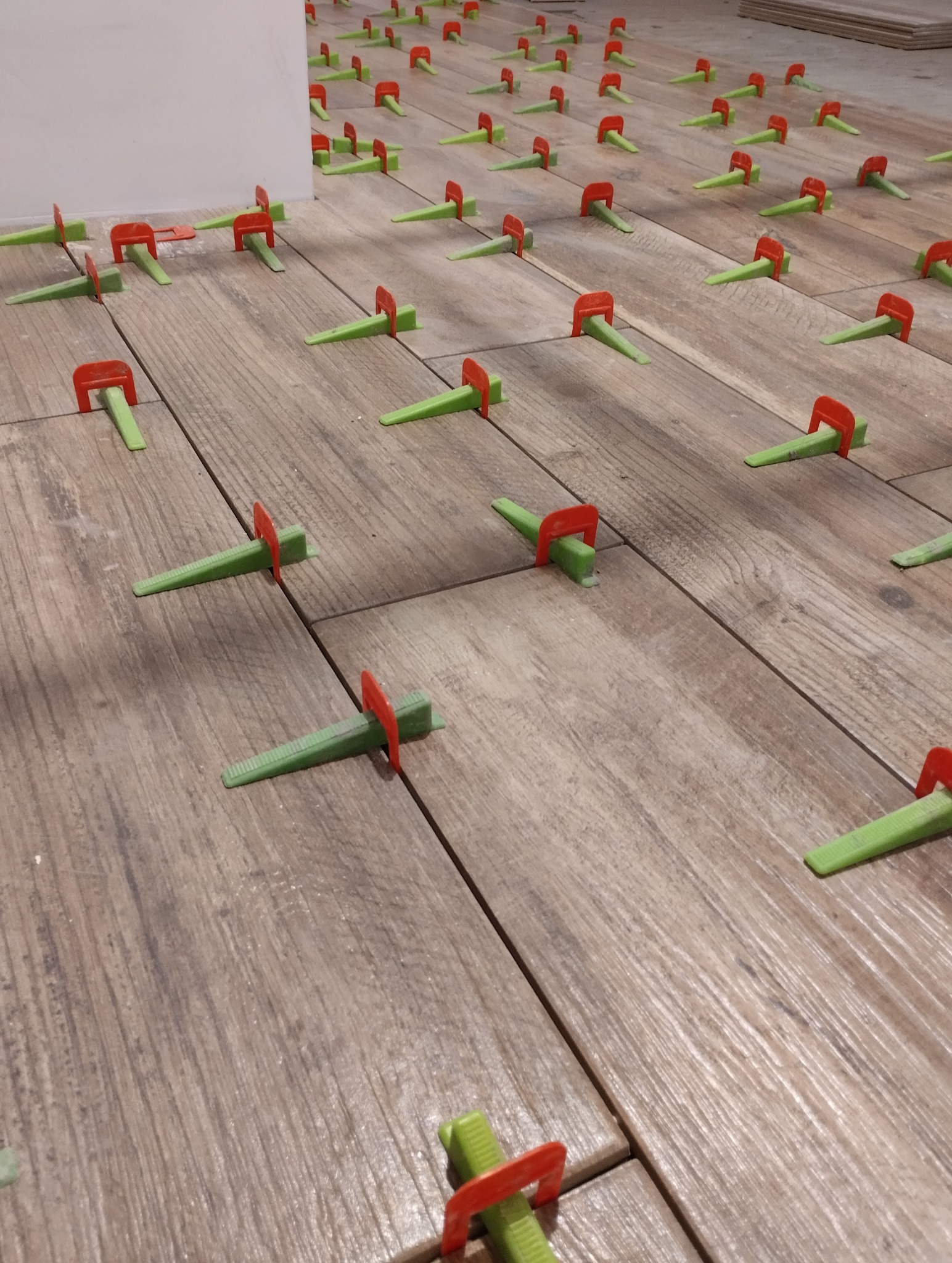 Ułożone płytki podłogowe z systemem poziomowania w Gliwicach. Widoczne zielone kliny i czerwone klipsy. Jasne, drewnopodobne płytki ułożone równo.