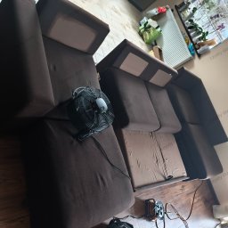 Pranie tapicerki meblowej Czysty Dom - Brązowa kanapa modułowa po czyszczeniu, z wentylatorem i przedłużaczem obok. Widok z góry, ukazujący detale tkaniny i efekt odświeżenia. Parkiet na podłodze.