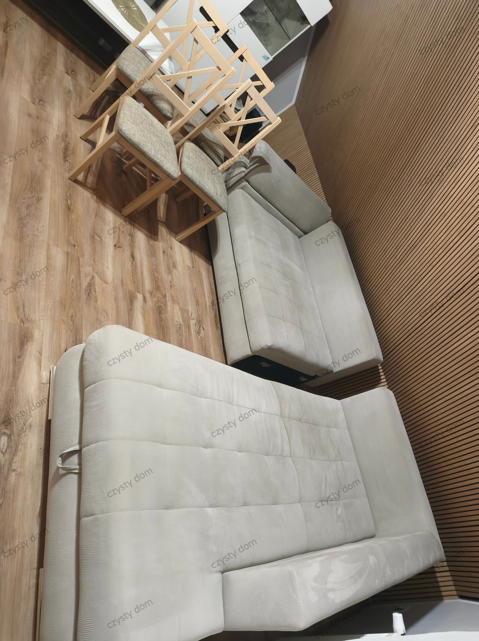 Jasnoszara, narożna kanapa z poduszkami i krzesła z drewnianymi nogami na drewnianej podłodze, widok z góry, po praniu tapicerki. Czyste meble w nowoczesnym wnętrzu.