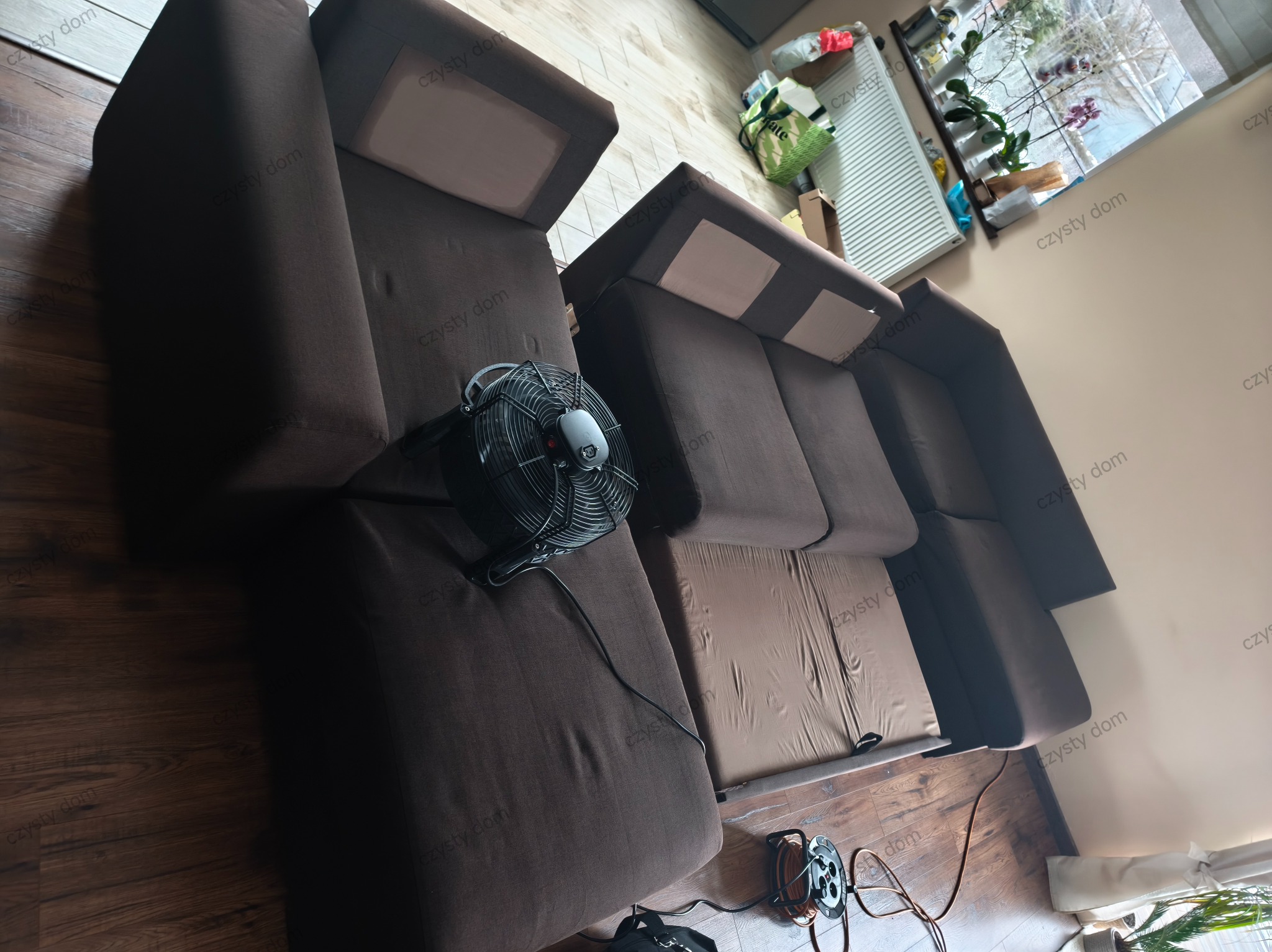 Brązowa kanapa modułowa po czyszczeniu, z wentylatorem i przedłużaczem obok. Widok z góry, ukazujący detale tkaniny i efekt odświeżenia. Parkiet na podłodze.