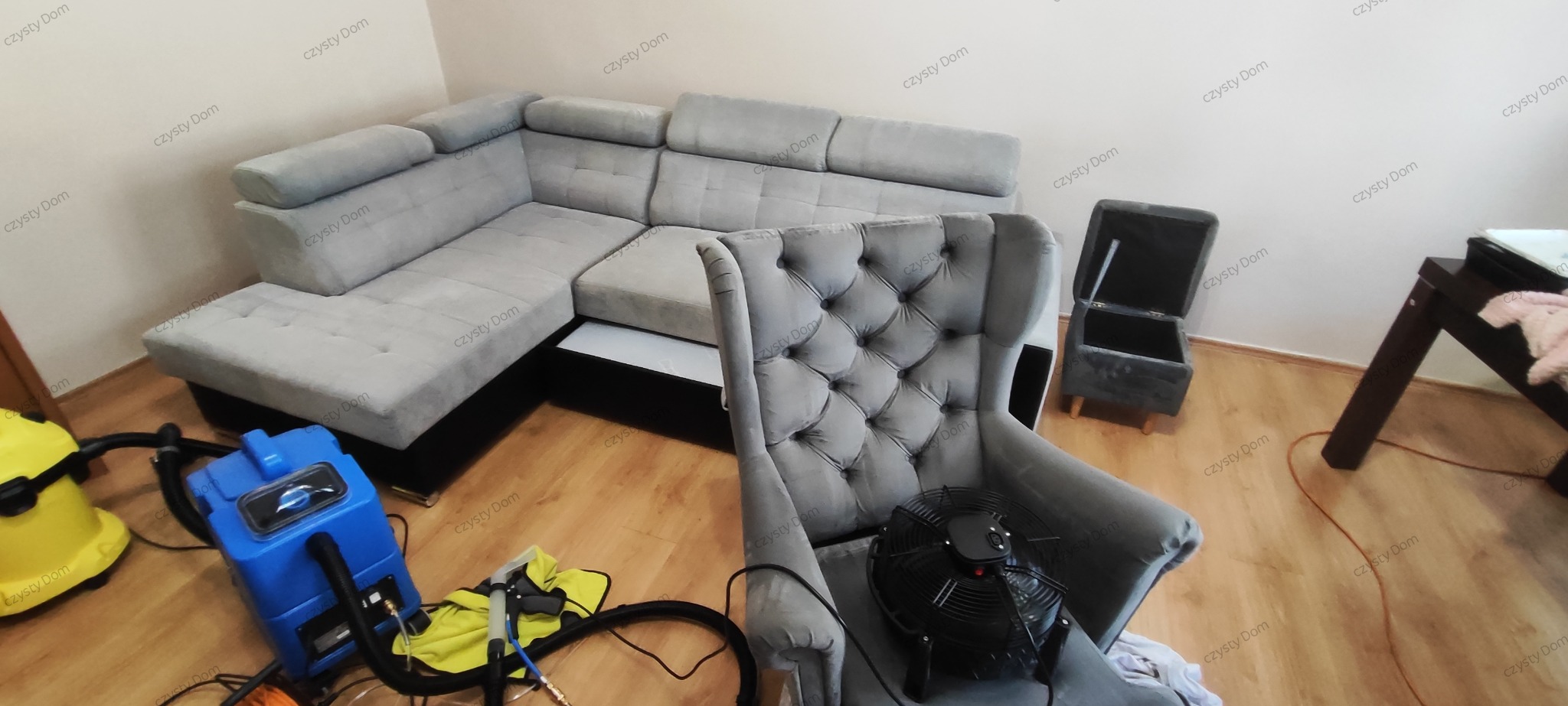 Szary narożnik i fotel przed suszarką po czyszczeniu. Widoczny sprzęt do prania tapicerki. Parkiet podłogowy. Ujęcie z góry, wnętrze mieszkania.