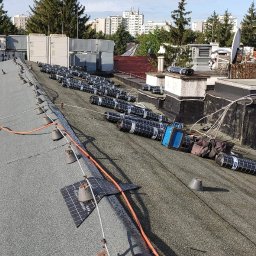 DACH SERWIS Łukasz Lewicki - Dach pokryty papą z przygotowanymi rolkami izolacji termicznej, widoczne elementy wentylacji i instalacji odgromowej. Prace dekarskie w toku, widok z góry.