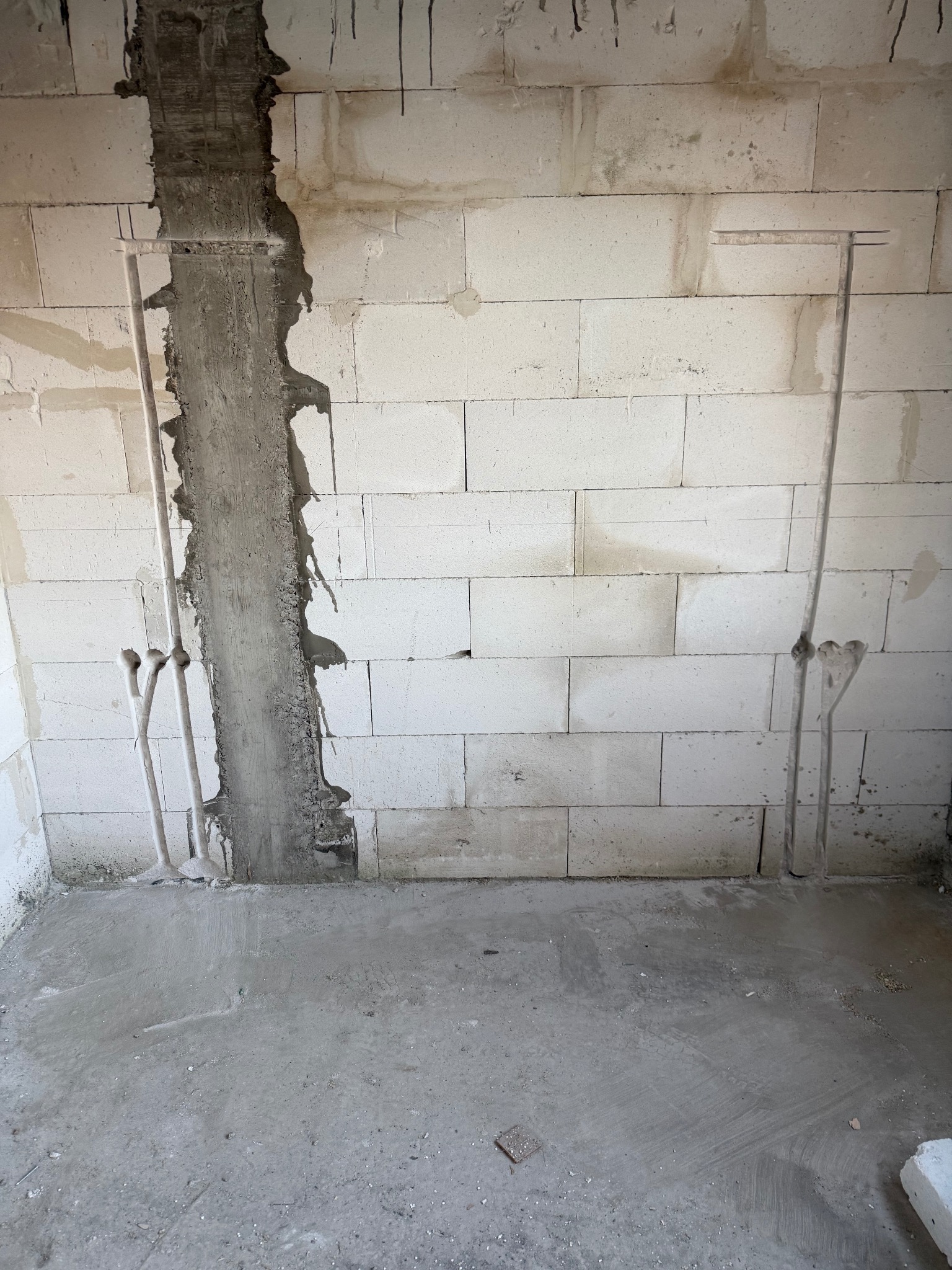 Ściana z betonu komórkowego z pionowymi bruzdami wypełnionymi zaprawą, w których umieszczono rury instalacji elektrycznej. Widoczne puszki instalacyjne.