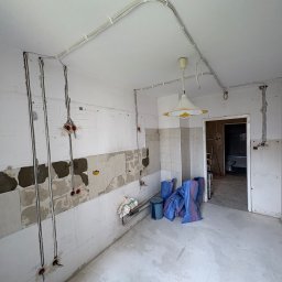 Damian Głąb - Kuchnia w trakcie remontu: widoczne kable elektryczne na ścianach i suficie, przygotowane do montażu gniazdek i oświetlenia. Częściowo usunięte płytki, worki z gruzem.