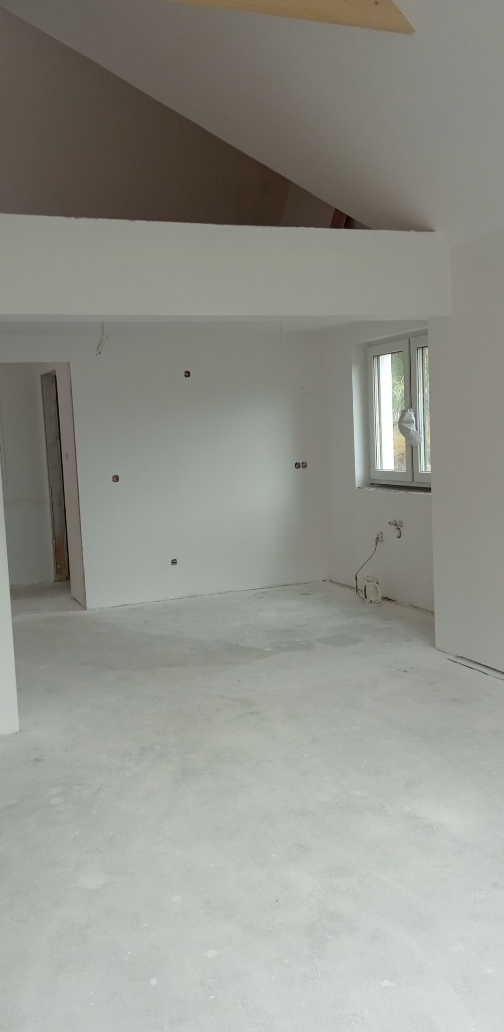 Wnętrze po gładziowaniu w Liniewie: białe ściany, surowy beton na podłodze, przygotowane do dalszych prac wykończeniowych, widoczne puszki elektryczne.