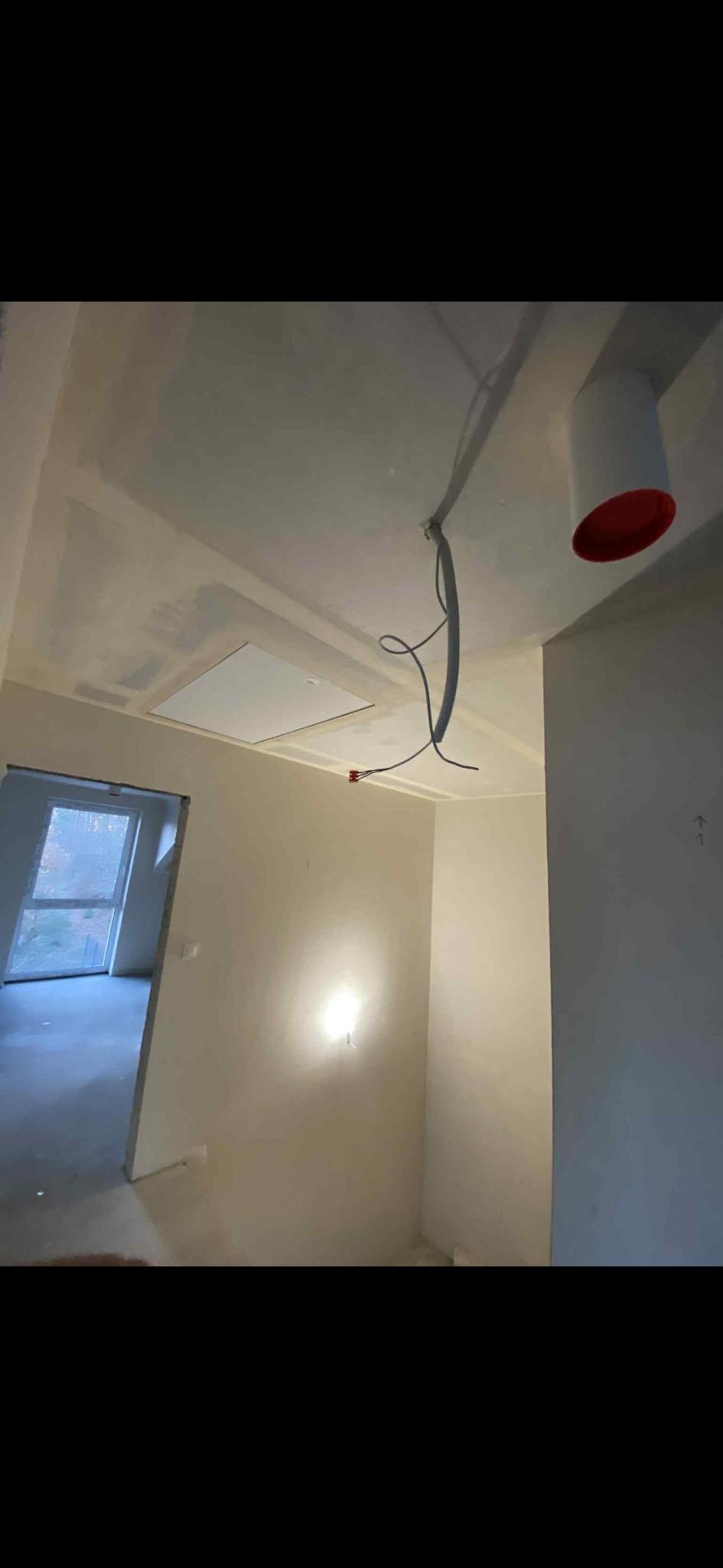 Wnętrze w trakcie prac wykończeniowych: ściany po szpachlowaniu, sufit z płyt karton-gips, widoczne przewody elektryczne i otwór rewizyjny. W tle okno.