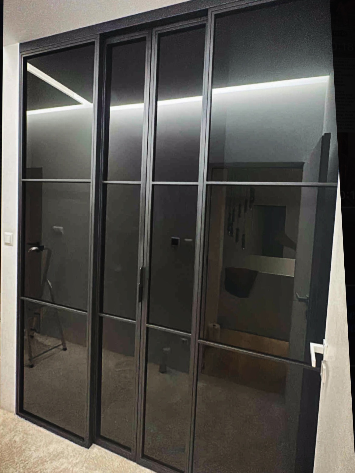 Nowoczesne, czarne, przeszklone drzwi przesuwne z metalową ramą, widoczne wewnątrz pomieszczenia z oświetleniem LED. Minimalistyczny design.