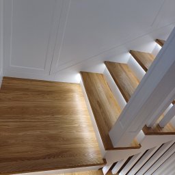 Karol Połom KPElektryk - Drewniane schody z białymi balustradami i podświetleniem LED, widok z góry. Nowoczesny design, jasne kolory, eleganckie wykończenie.