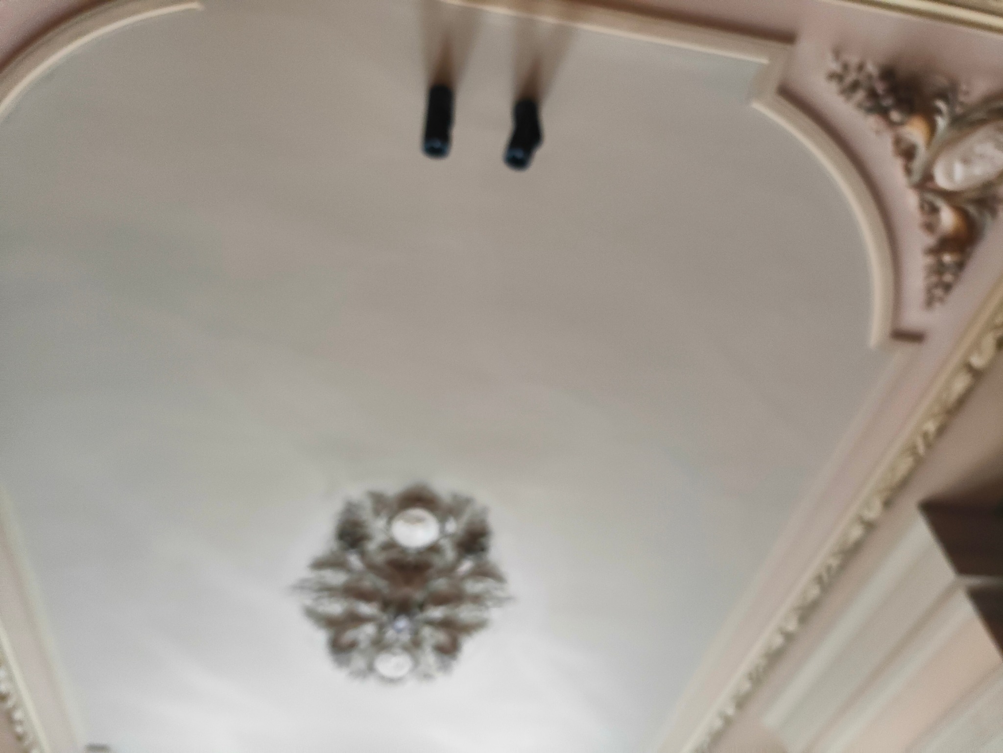 Ozdobny sufit w stylu retro z rozetą i sztukaterią w odcieniach beżu i bieli. Widoczne elementy oświetlenia. Ujęcie z dołu.