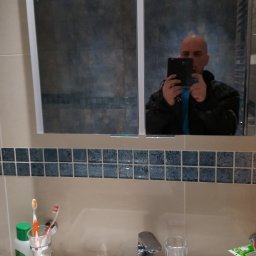 BEBEK, BEBEK MAN BUŁKA I SPÓŁKA DARIUSZ LENART - Łazienka z umywalką, baterią i lustrem, w którym odbija się osoba robiąca zdjęcie telefonem. Widoczne płytki dekoracyjne i akcesoria łazienkowe.