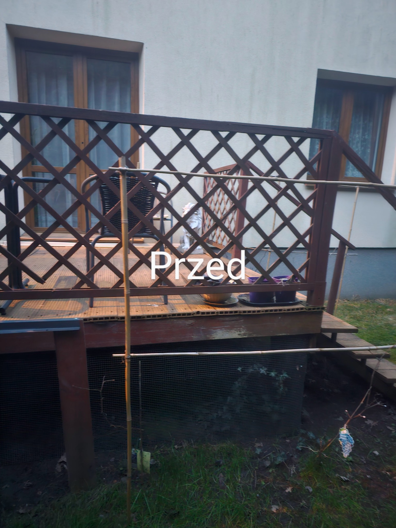 Drewniany taras z kratownicą w Jazgarzewszczyźnie, widok 'przed' remontem. Widoczne meble ogrodowe i rośliny w donicach. Ujęcie z dołu, w tle ściana budynku.