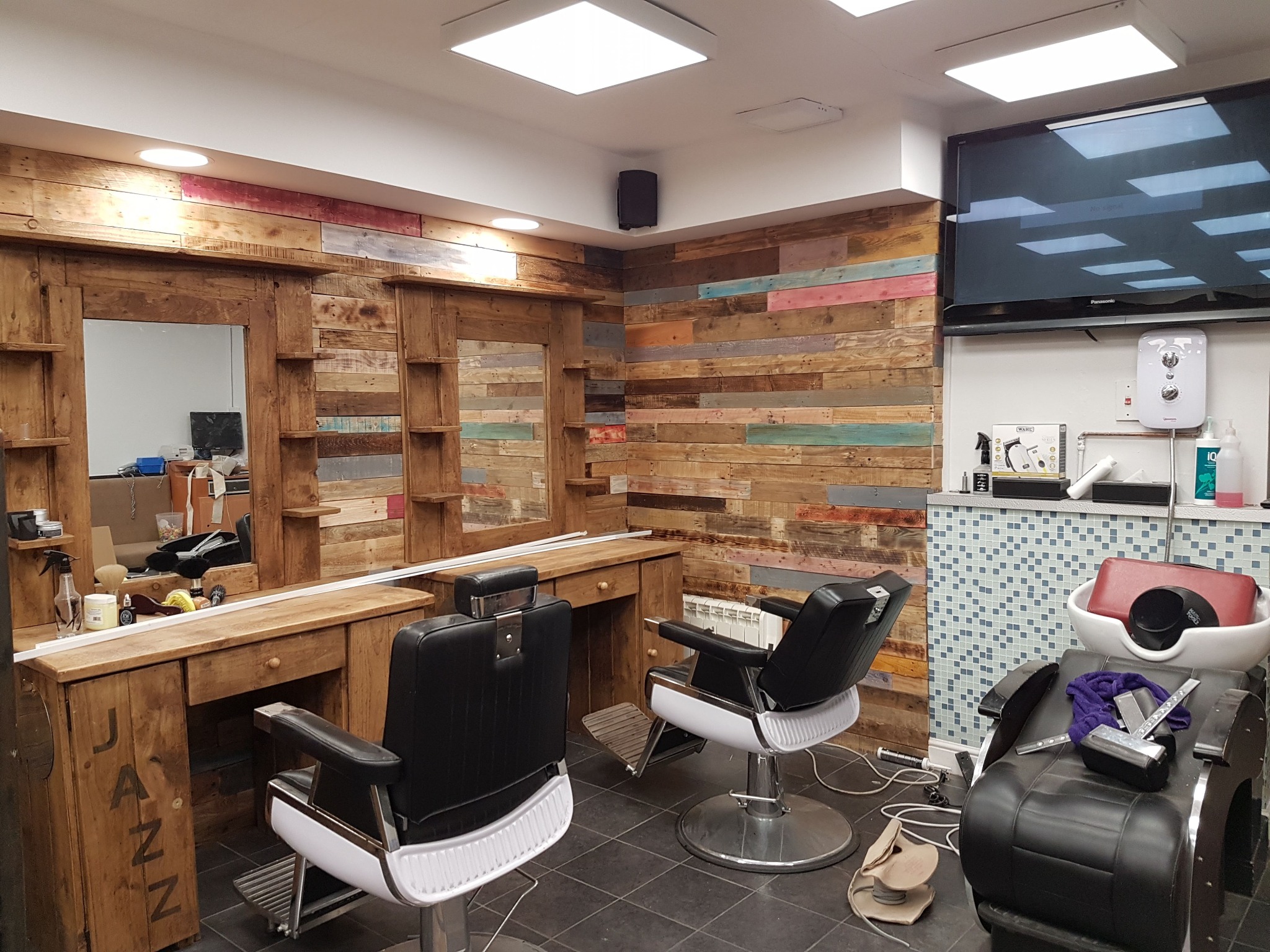 Nowoczesne wnętrze salonu fryzjerskiego z drewnianymi elementami dekoracyjnymi na ścianach i meblach. Dwa fotele fryzjerskie i stanowisko do mycia włosów.