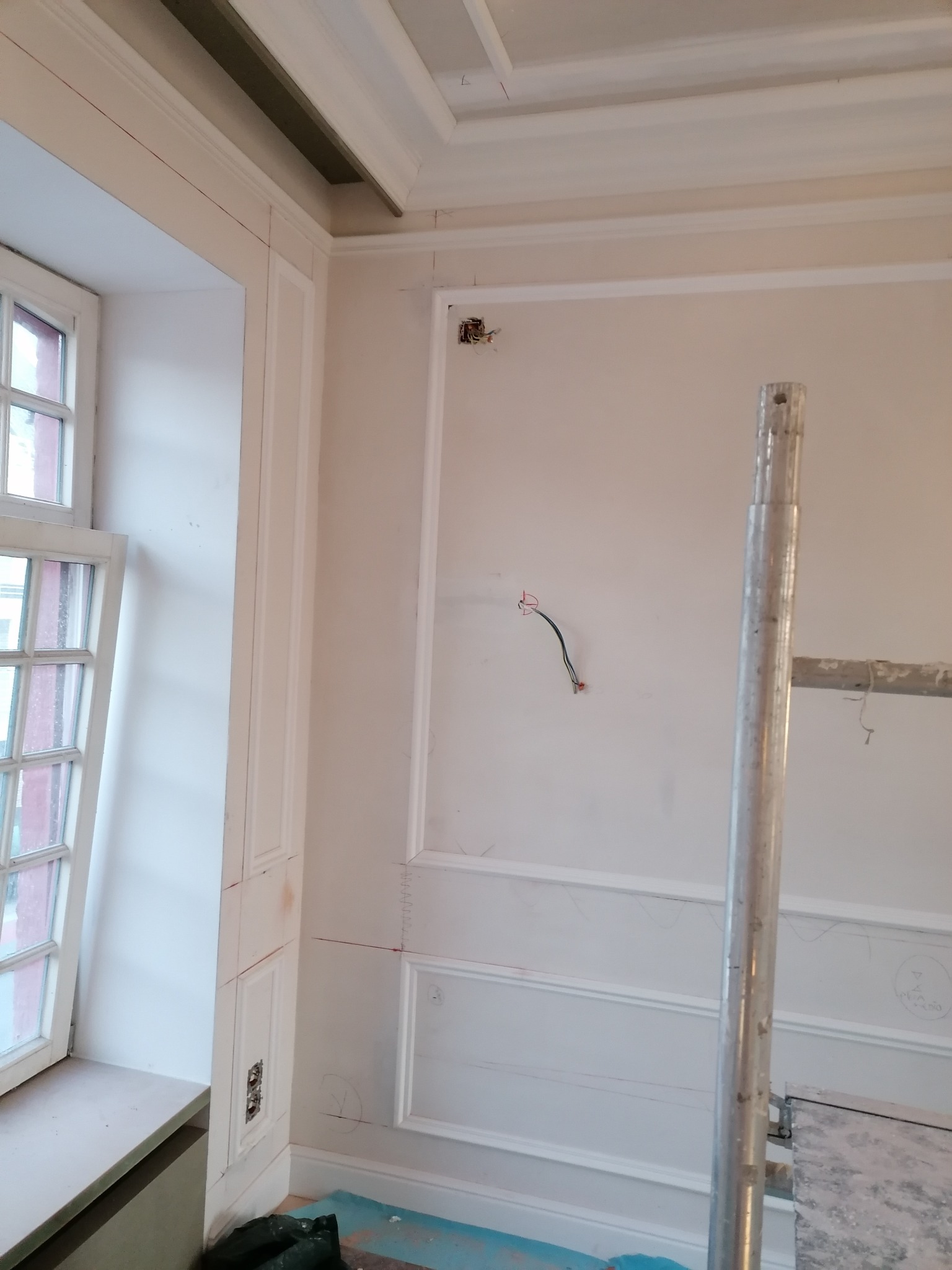 Wnętrze w trakcie prac wykończeniowych: ściany z dekoracyjnymi listwami, widoczne przewody elektryczne, rusztowanie. Przygotowanie do malowania.